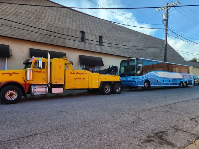 Universal Towing professional yellow tow truck transporting blue bus in Baltimore MD